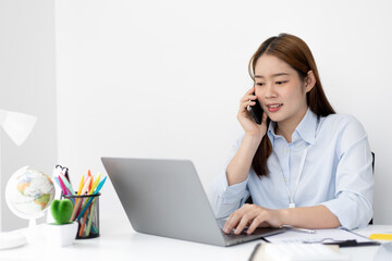 Asian female employee talking on the phone and working in a laptop with a smiling face, Office staff work and telephone conversations, Business conversation over the phone.