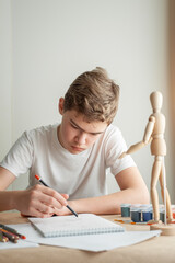 Naklejka premium A teenage Caucasian boy learns to draw. A boy draws a man on a model. Creative hobby. Drawing lesson.