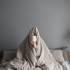 Woman sitting in bed, holding mug with coffee in hand. Happy morning breakfast concept. Freelancer,...