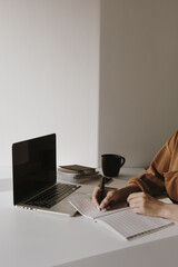 Minimalist home office workspace with laptop, coffee cup, clipboard. Woman write in a paper sheet...