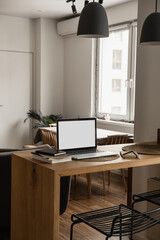 Laptop computer with blank screen, notebooks on wooden table in warm sunlight room. Aesthetic minimal interior design template with mockup copy space. Blog, web, social media concept.