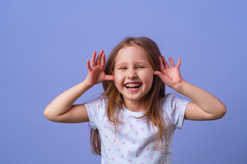 Little girl 5 years old with blonde hair in a T-shirt with colored polka dots standing happily smiling on purple background. Close-up. the model is having fun and feels overwhelmed, amazed.