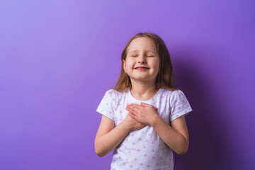 little girl with her eyes closed holds her hands on chest, feels grateful, child dreams with...