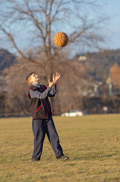 Young Boy Throwing Basketball Ball Up In The Air.  Teenager Playing With Basketball Ball In The Park
