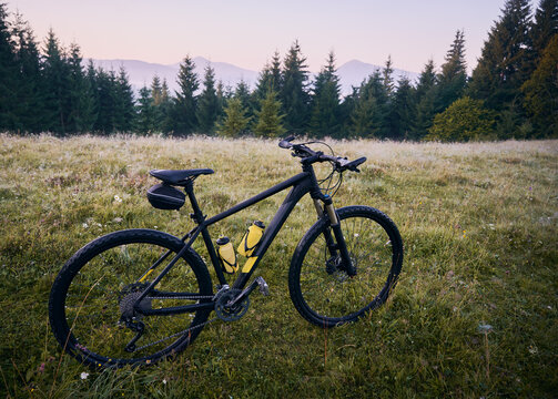 Grassy hill with multi-speed touring bicycle with yellow water bottles in cages. Mountain bike or cycle on grass with coniferous trees and hills on background. Concept of mountain biking.