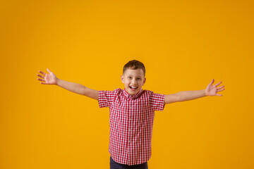 cheerful boy of about 8 years old in a red checkered shirt spread his arms out to the sides and smiled happily on yellow background. Close-up. boy rejoices in success and victory. Discounts and sales
