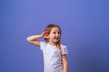 charming little girl smiles with her hand over her ear while listening and hearing rumors or gossip...
