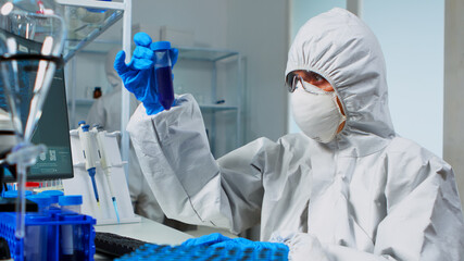 Researcher in coverall testing liquid sample using test tubes for new treatment medical laboratory....