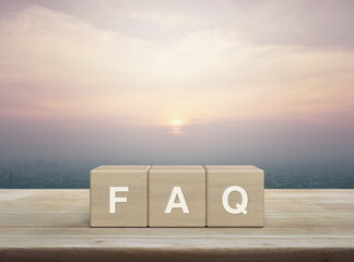 FAQ letter on block cubes on wooden table over city tower and skyscraper at sunset, vintage style,...