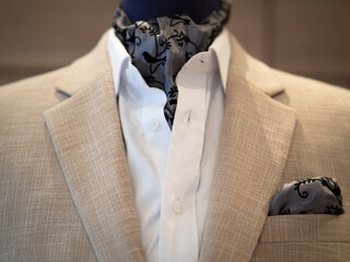 Close up of beige jacket suit with white shirt and ascot tie scarf on mannequin. selective focus - obrazy, fototapety, plakaty