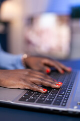 Side view of african woman hands typing on laptop working on deadline for company. Employee using modern technology network wireless doing overtime.