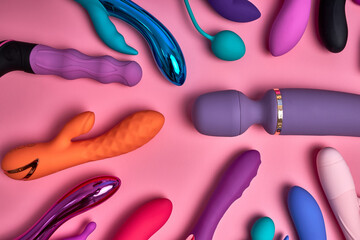sex shop's erotic toys on pink background, many colourful different dildos and silicone vibrators...