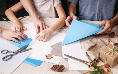 Hands of a caucasian girl and her brother are cutting paper snowflakes with scissors. Handmade, christmas decorations, family winter activity. Close-up.