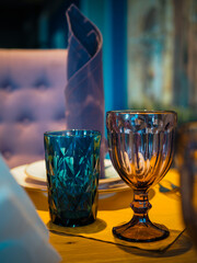 Close-up of a blue glass and a purple goblet made of thick glass in a stylish interior on a ginger table on a blue-purple background