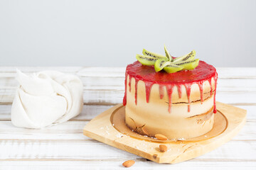 Gluten-free cake with strawberry frosting, coconut chips and almonds on a stand, on a wooden table, on light background. Copy space.