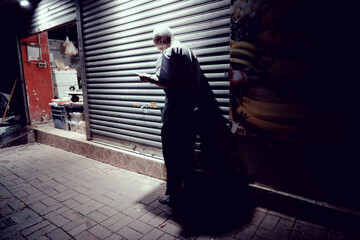 An old man stands outside of a shopfront at night in Hong Kong