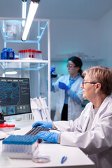 Senior doctor in white coat working on computer in discovery laboratory. Microbiology research and analysing in science medicine lab developing and stying new type of vaccin