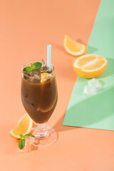Cold coffee with ice, orange and mint in a glass glass on a bright background with a shadow.