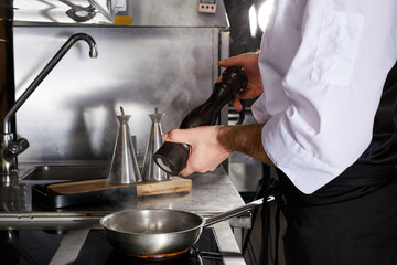 Chef add spices to dish cooking on fire, on stove. Cropped male cook in apron during preparing dish, in restaurant kitchen