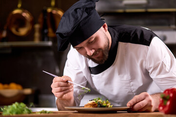 Chef finishing dish on plate with dish dressing and almost ready to serve at table, adding some zest, professionally cooked and decorated meal for restaurant visitors