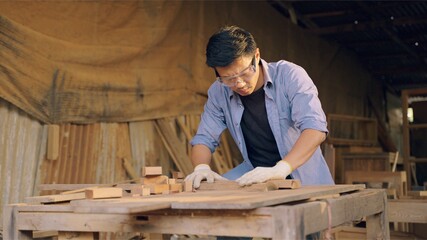 Carpenter working on wood craft at workshop to produce construction material or wooden furniture. The young Asian carpenter use professional tools for crafting. DIY maker and carpentry work concept.