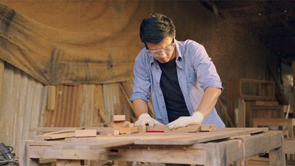 Carpenter working on wood craft at workshop to produce construction material or wooden furniture. The young Asian carpenter use professional tools for crafting. DIY maker and carpentry work concept.