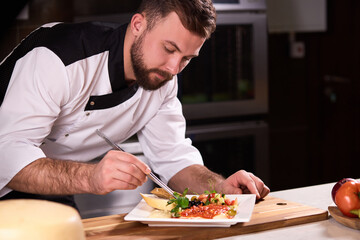 chef carefully completes preparation of dish, adds missing ingredients, professional cooking in restaurant by male cook in apron