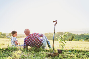 Grandfather and grandson sitting in the meadow at sunset