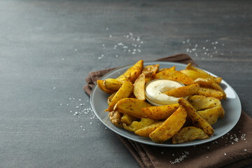 Plate with potato wedges and sauce on dark textured background