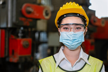 woman engineering wear protection face mask and safety helmet holding standing front machine in factory Industrial. new normal work during epidemic covid-19.