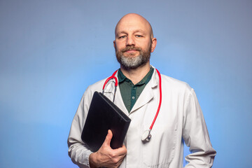 Bald doctor with beard on a blue background. The model is in his 40s. Looking at a open folder. Wearing white uniform. Holding black folder.