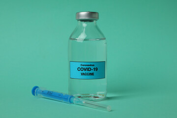 Vial of Covid - 19 vaccine and syringe on mint background