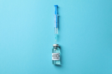 Vial of Covid - 19 vaccine and syringe on blue background