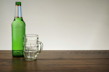 Green beer bottle and empty glass on a wooden table and bright background. Copy space