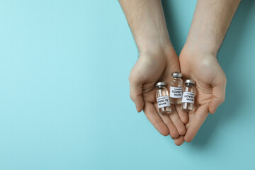 Male hands hold vials of Covid - 19 vaccine on blue background