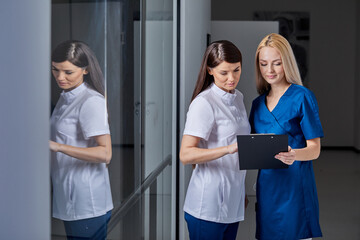 Two Young Professional Medical Workers In Unifrom Discussing Tasks Ways To Treat Patient, Read Information About Diagnosis In Clipboard, In Hospital