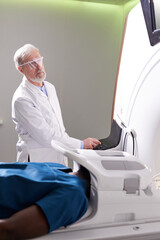 Male Patient Lying On MRI Machine While Elderly professional Doctor Operating It, Radiologist in White Medical Suit Treating Patient, Examining Health