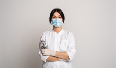 Female doctor or scientist wearing protective facial mask standing with crossed arms over grey background