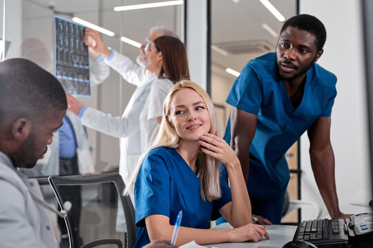 Interracial radiologists sitting at table in front of computer monitors with x-ray images and pleasantly discussing diagnosis in team at office. medicine concept
