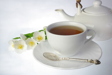 Obraz na płótnie Canvas White faience tea cup, teapot and jasmine flowers.