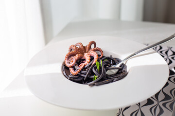Octopus with black pasta in white plate.