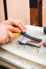 The hand with the stationery knife cuts off part of the leather blank. The chisel is on the table next to the stumps of the skin.