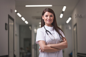Portrait of confident female Doctor posing at camera in hospital hall, having pleasant look. good-looking woman in uniform with stethoscope indoors