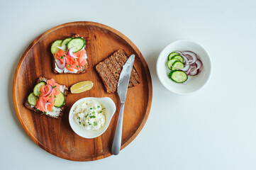 tasty diet food for breakfast or brunch - avocado and salmon toast with cream cheese, cucumber and red onion served on wooden plate