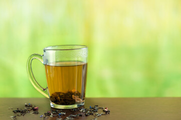 Transparent mug with hot flower tea on a delto green background. Selective focus. Natural lighting with copy space for text