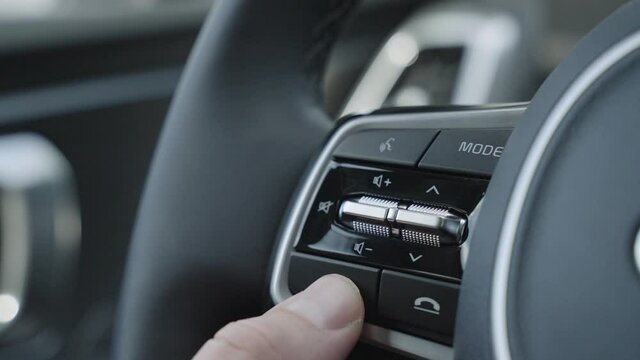 Close up of finger pressing the audio control buttons to increase or decrease the volume on the steering wheel when driving. Steering wheel audio volume adjust