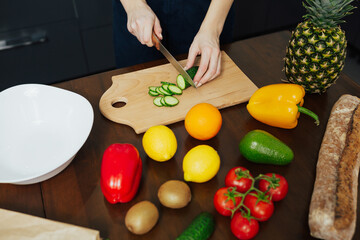 Woman's hands cut cucumber, cooking healthy fresh salad in the kitchen. Healthy food.