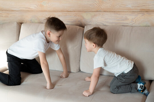 Two boys playing together, sitting on sofa in confrontation position at home, wooden house