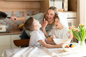 Obraz na płótnie Canvas happy family concept: mom plays and cooks easter dinner with her sons at home in sunny day