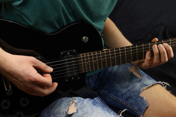 Fototapeta na wymiar man sitting down plays a black electric guitar